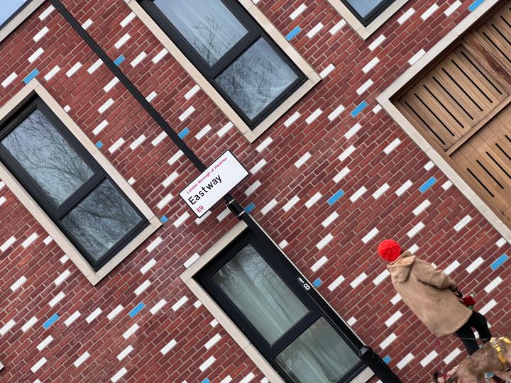 A person walks a dog in front of a building with red brickwork, with alternating diagonal bricks white and blue.