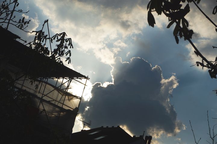 A dark grey cumulus cloud in dense, mixed fluffy clouds, with a silver lining, foreground silhouetted houses & trees