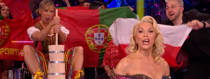 Hannah Waddingham hosts the Eurovision Song Contest. In the background, Mel Giedroyc churns butter in a Polish dress.